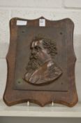 A relief cast bronze plaque of Dickens on an oak panel.
