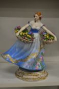 A continental porcelain figure of a lady with a basket of flowers in each hand.
