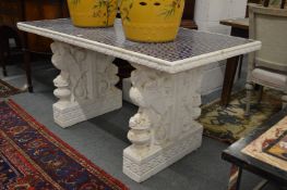 A tile top table with a pair of ornate cast composite and painted supports.