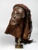 A CARVED WOOD AFRICAN MASK, with naturalistically plated sea grass hair, on later stand Mask 8ins
