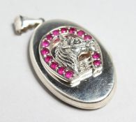 A SILVER AND RUBY OVAL LOCKET with horse head and horse shoe decoration, 1.5ins high.