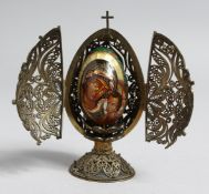 A RUSSIAN FILIGREE SILVER FOLDING EGG SHAPED FRAME, containing a porcelain egg with cross and