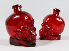 A PAIR OF UNUSUAL RUBY COLOURED GLASS SKULL SHAPED BOTTLES. 6.5ins high.