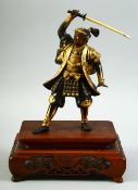 A JAPANESE GILDED BRONZE OKIMONO, of a samurai standing figure, his right arm held aloft holding a