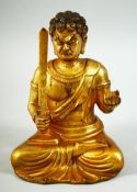 A GILT BRONZE MODEL OF A SEATED DEITY, sitting with legs crossed holding a sword in one hand and