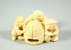 A JAPANESE CARVED IVORY NETSUKE, depicting three crouching figures surrounding an open oven or