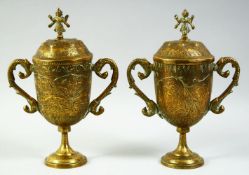 A PAIR OF INDIAN ENGRAVED AND CHASED BRASS LIDDED PEDESTAL CUPS, with twin handles, the lids with