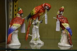 A Naples porcelain model of a parrot on a tree stump together with a pair of similar parrots.