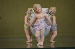 A small Dresden vase modelled as three cherubs holding an urn.