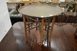An eastern engraved brass circular tray on folding bamboo stand.