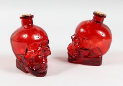 A PAIR OF GLASS SKULL DECANTERS with red overlay 6ins high.