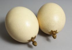 A PAIR OF OSTRICH EGGS each with an ormolu pineapple form finial.`