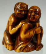 A JAPANESE CARVED AND STAINED IVORY NETSUKE of a crouching man and an oni, 4cm high.