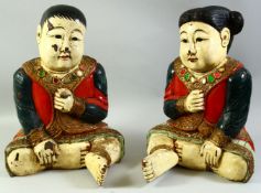 A LARGE PAIR OF POLYCHROME DECORATED WOODEN FIGURES of seated Chinese children, 47cm high.