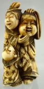 A JAPANESE CARVED IVORY NETSUKE of a man holding a mask, an inquisitive child at his feet, signed to