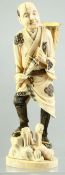 A JAPANESE CARVED IVORY OKIMONO of a man standing on a rocky outcrop with a basket on his back,