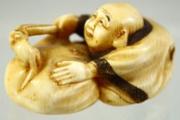 A JAPANESE CARVED IVORY NETSUKE of a seated man playfully teasing a mouse in a basket, signed to the