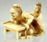 A JAPANESE CARVED IVORY NETSUKE of a man leaning on a table; his back being massaged by a young