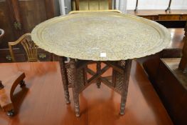 An eastern brass tray table together with another circular engraved brass tray and an embossed