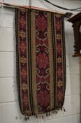 An eastern textile wall hanging with carved wood wood hanging pole.