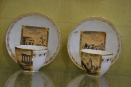 A pair of French porcelain cups and saucers painted with landscapes.