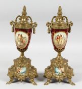 A PAIR OF 19TH CENTURY GILT METAL AND PORCELAIN URNS painted with figures with pineapple finials and