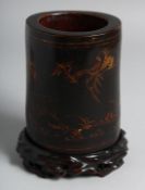 A CHINESE LACQUERED BAMBOO BRUSH POT on a fitted hardwood stand, decorated with deer and crane.