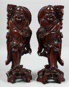 A PAIR OF CHINESE CARVED HARDWOOD FIGURES, raised on pierced hardwood bases, each with inset eyes,