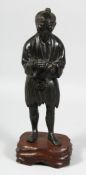 A JAPANESE MEIJI PERIOD BRONZE FIGURE of a man holding a pipe, mounted on a carved hardwood base,