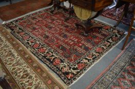 A Persian rug, red ground with four rows of seven square shaped panels decorated with stylized