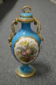 A decorative porcelain twin handled vase and cover, blue ground decorated with panels of fruit.
