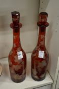 A pair of ruby glass bottle decanters engraved with grapes and vines (1 small rim chip).