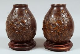 A PAIR OF JAPANESE HEAVY BRONZE VASES with hardwood stands, with relief floral decoration, the bases