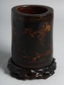 A CHINESE LACQUERED BAMBOO BRUSH POT on a fitted hardwood stand, decorated with deer and crane.