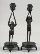 A PAIR OF JAPANESE BRONZE CANDLESTICKS, formed as figures holding the candle cup aloft, 27.5cm