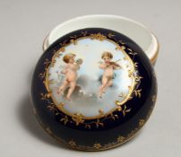 A SMALL BERLIN CIRCULAR BOX AND COVER, blue ground painted with cupids. 3.25ins diameter.