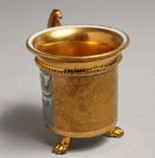 A 19TH CENTURY BERLIN GILT GROUND CUP on three claw feet.