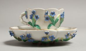 AN AUGUSTUS REX FLOWER ENCRUSTED CUP AND SAUCER. Mark 'A R' in blue.
