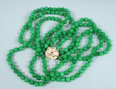 A STRING OF JADE BEADS, triple row with gold, ruby and diamond clasp.