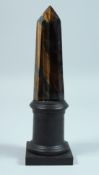 A TIGER'S EYE OBELISK on a wooden base. 8.5ins high.