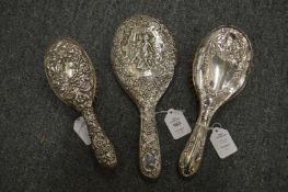 An embossed silver backed dressing table hand mirror together with two similar brushes.