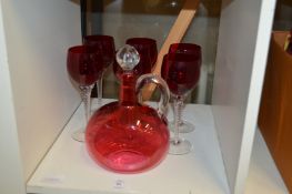 A cranberry glass claret jug and six ruby glass wine glasses.
