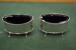 A pair of silver oval shaped salts with blue glass liners.