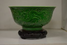A Chinese green ground porcelain bowl with moulded dragon decoration on a hardwood stand.