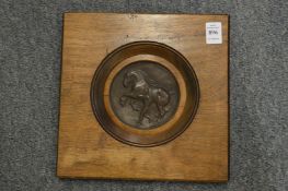 A circular bronze plaque depicting a horse and handler mounted in a mahogany frame.