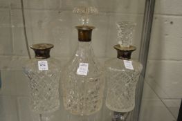 A pair of cut glass decanters with silver collars and a similar decanter (lacking one stopper).