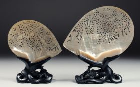 TWO CHINESE CARVED AND PIERCED MOTHER OF PEARL SHELLS on hardwood stands, the larger depicting