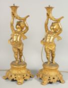 A GOOD PAIR OF FRENCH GILDED METAL CUPID LAMPS with glass domes. 19ins high.