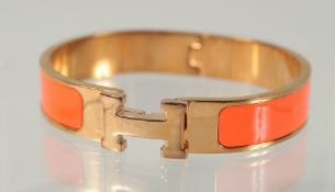 A HERMES ORANGE AND CHROME BANGLE.