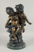AFTER A. MOREAU A TWO COLOUR BRONZE OF TWO CHERUBS on a circular marble base. 1ft 9ins high.